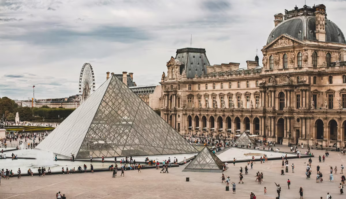Visitors walk around the Louvre glass pyramid and museum courtyard in Paris.