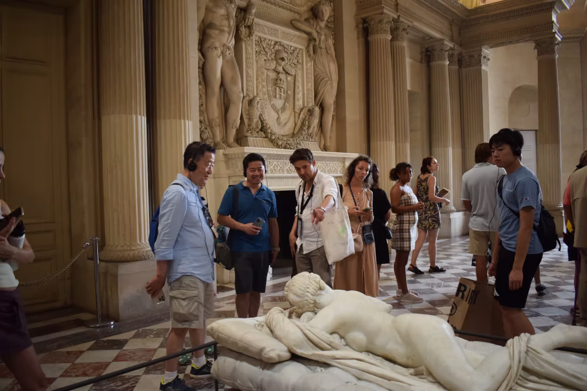A guide shows visitors a marble sculpture inside the Louvre Museum.