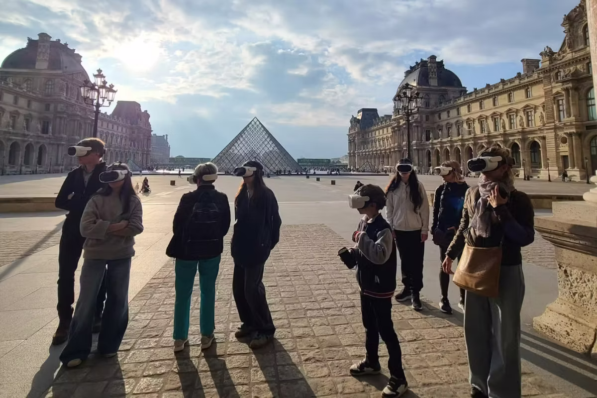 Visitors use VR headsets during a tour in the Louvre courtyard near the glass pyramid.