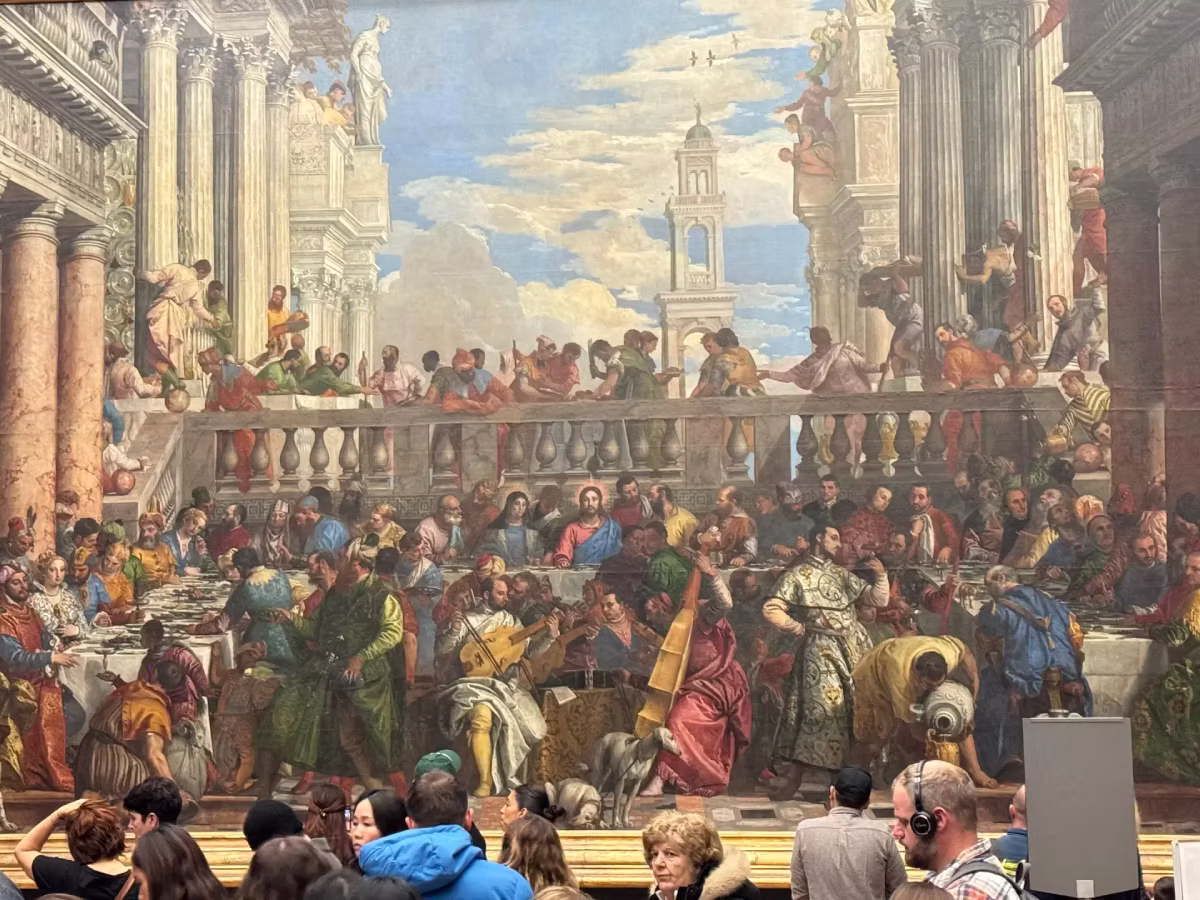 Visitors view The Wedding Feast at Cana painting inside the Louvre Museum.